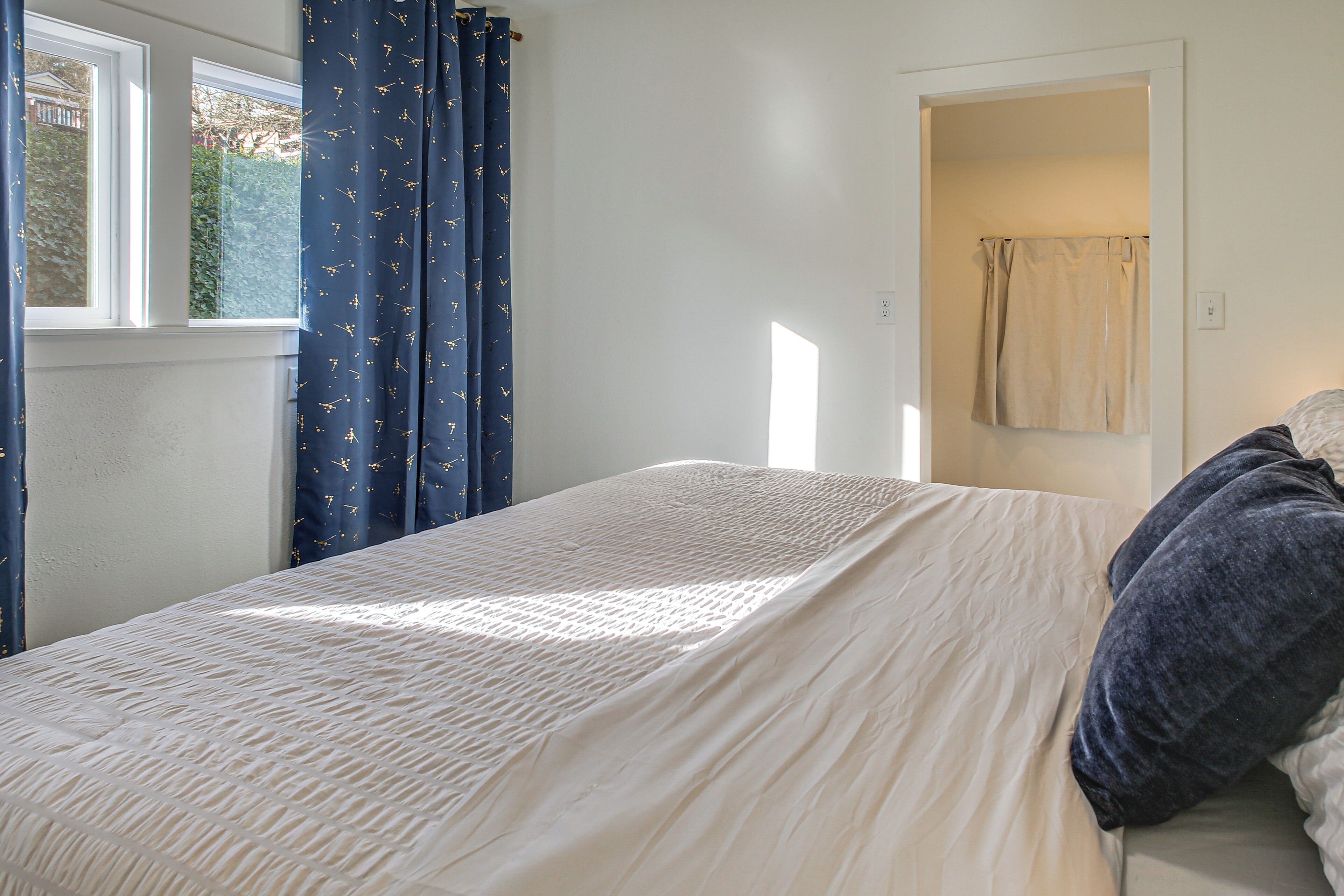 A bedroom with a bed, a window with curtains, a door, and a light switch on the wall.
