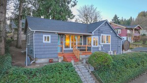 Une maison à deux étages avec un porche, un escalier menant à la porte d’entrée et un jardin bien entretenu.