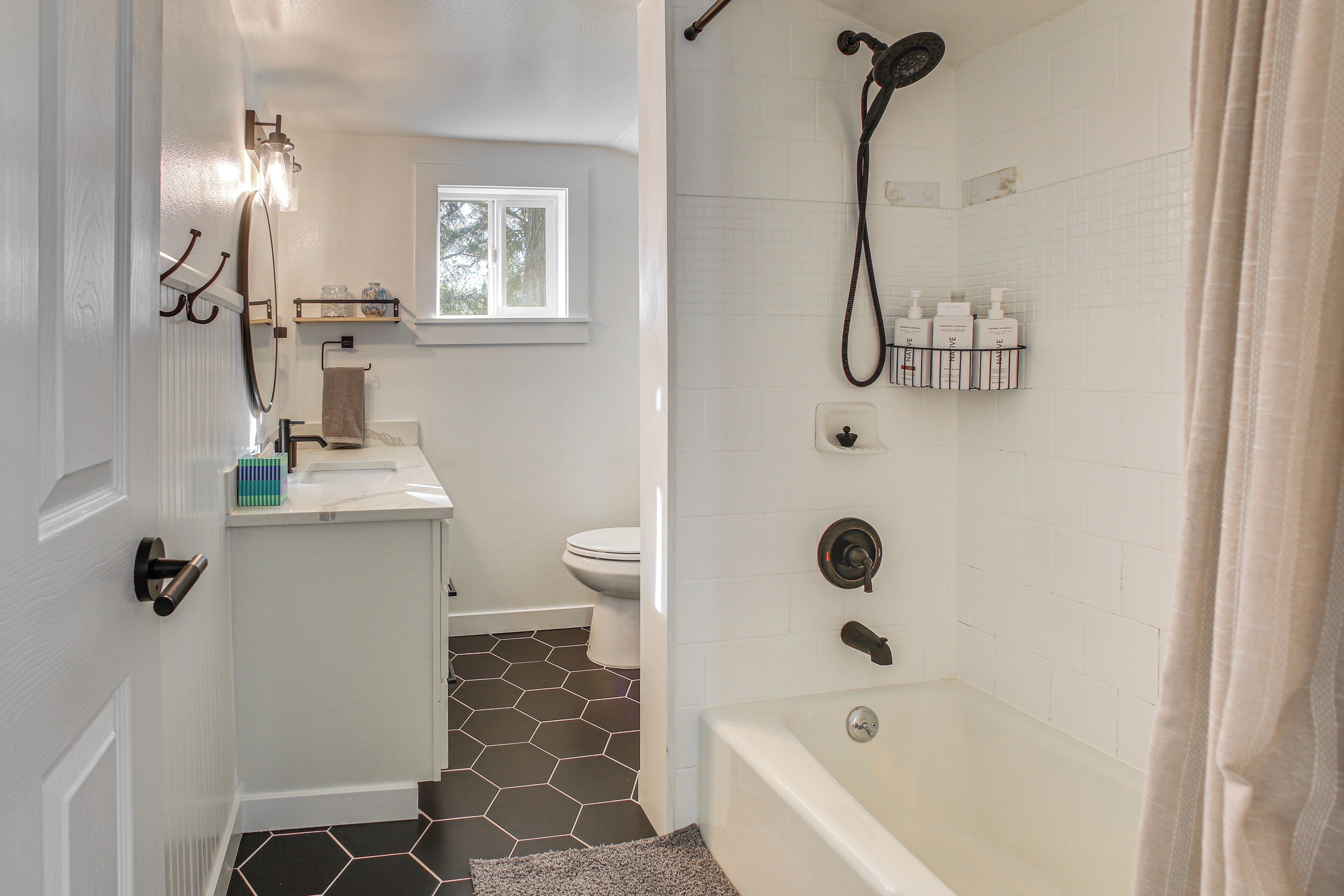 Ein Badezimmer mit Dusche, Toilette und Waschbecken, mit weiß gefliesten Wänden und einem sechseckigen Bodenmuster.