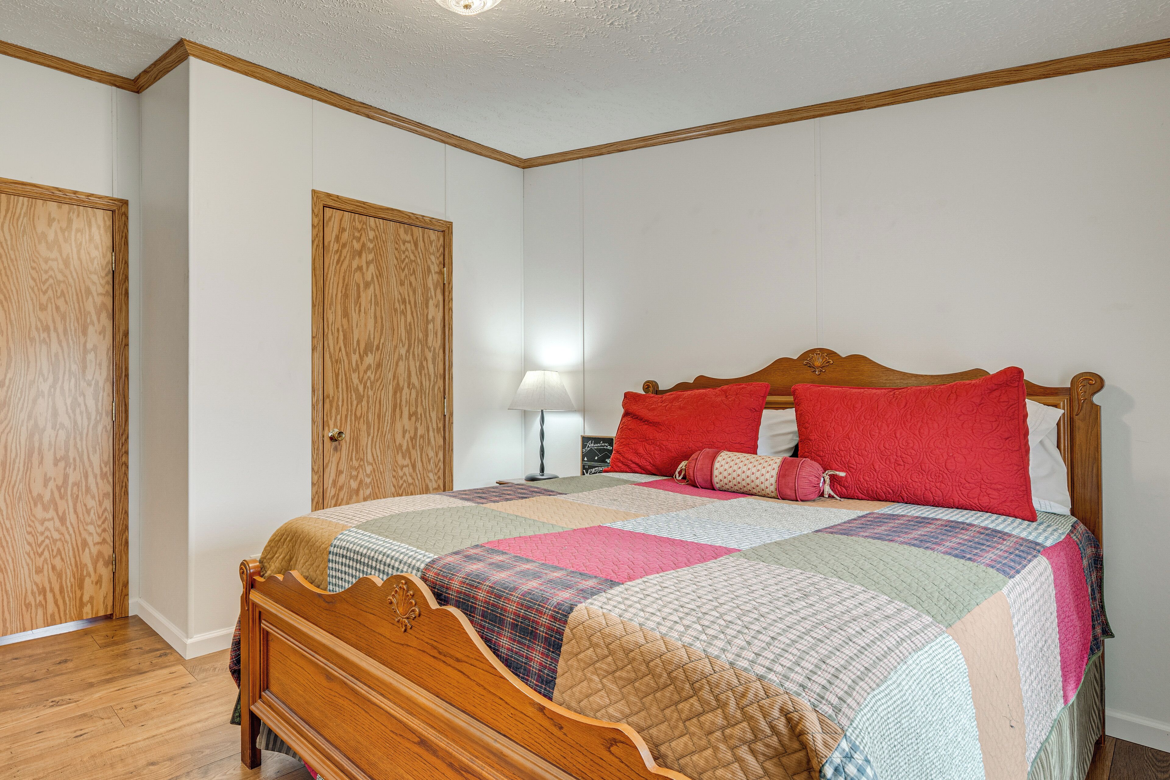 A bedroom with a wooden bed, a quilt, a nightstand, a lamp, and a wardrobe.