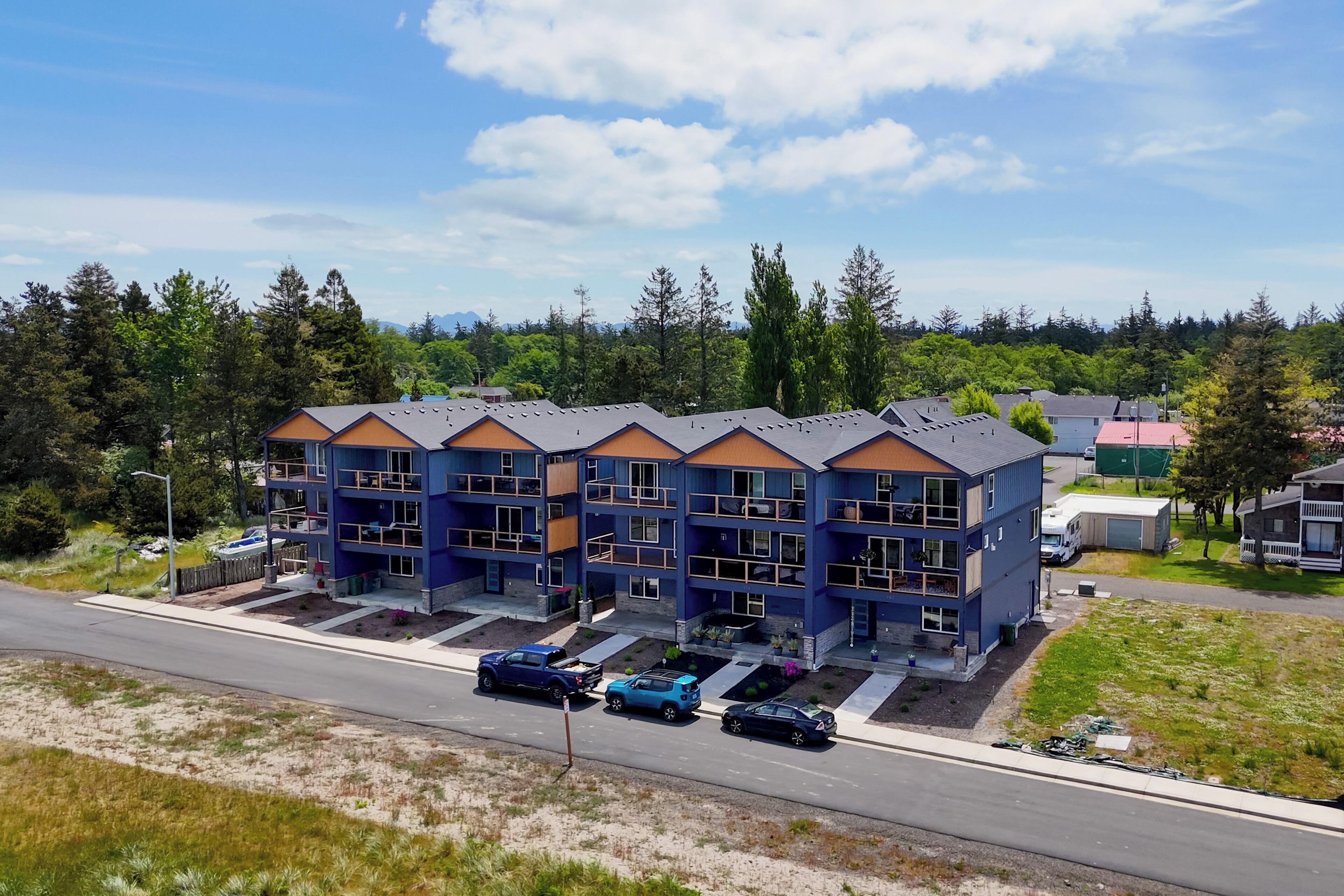 Un immeuble résidentiel à plusieurs étages, doté de balcons, d’un espace de stationnement et d’une route au premier plan.