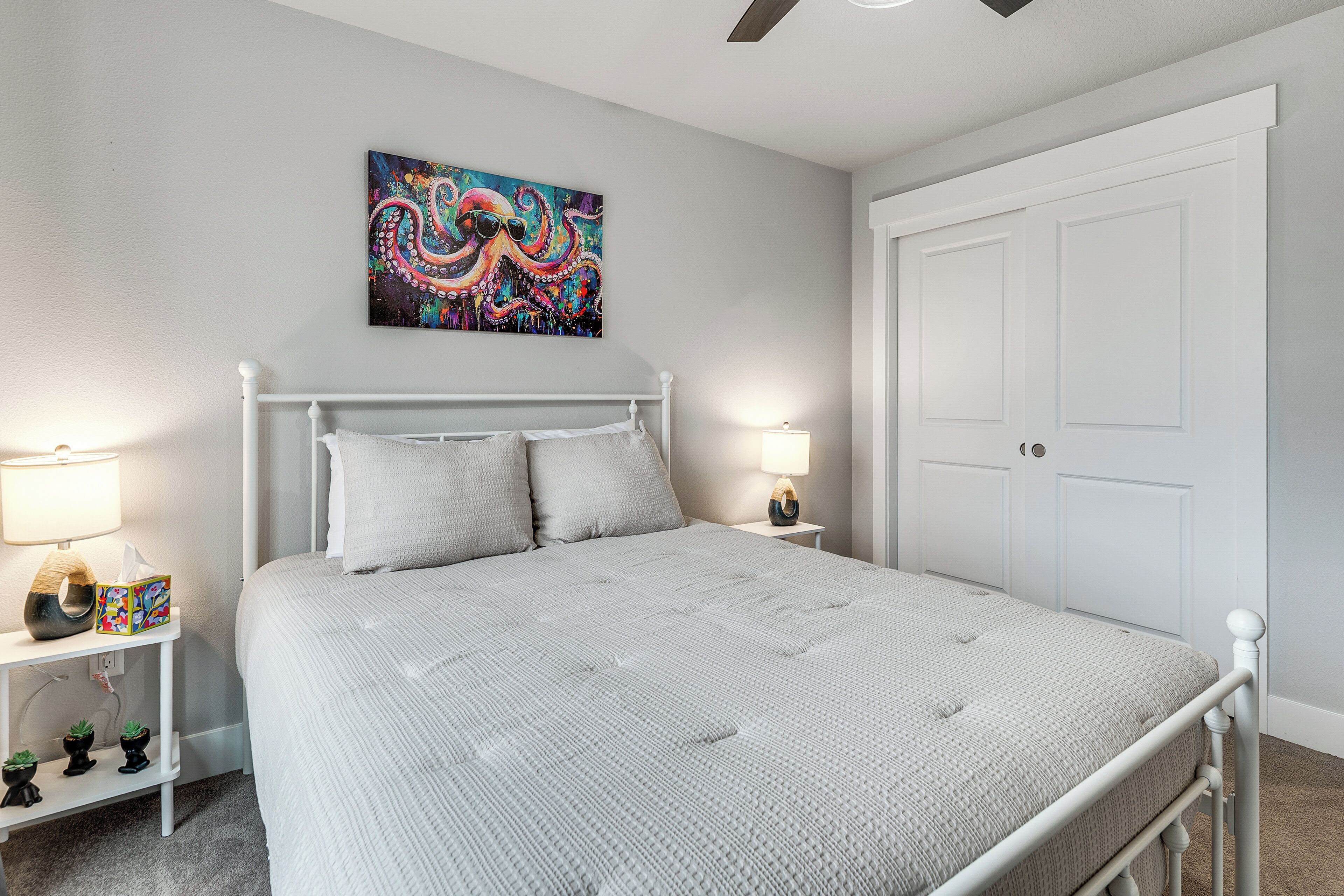 A bedroom with a bed, bedside lamps, a nightstand, a wall art piece, and a door.