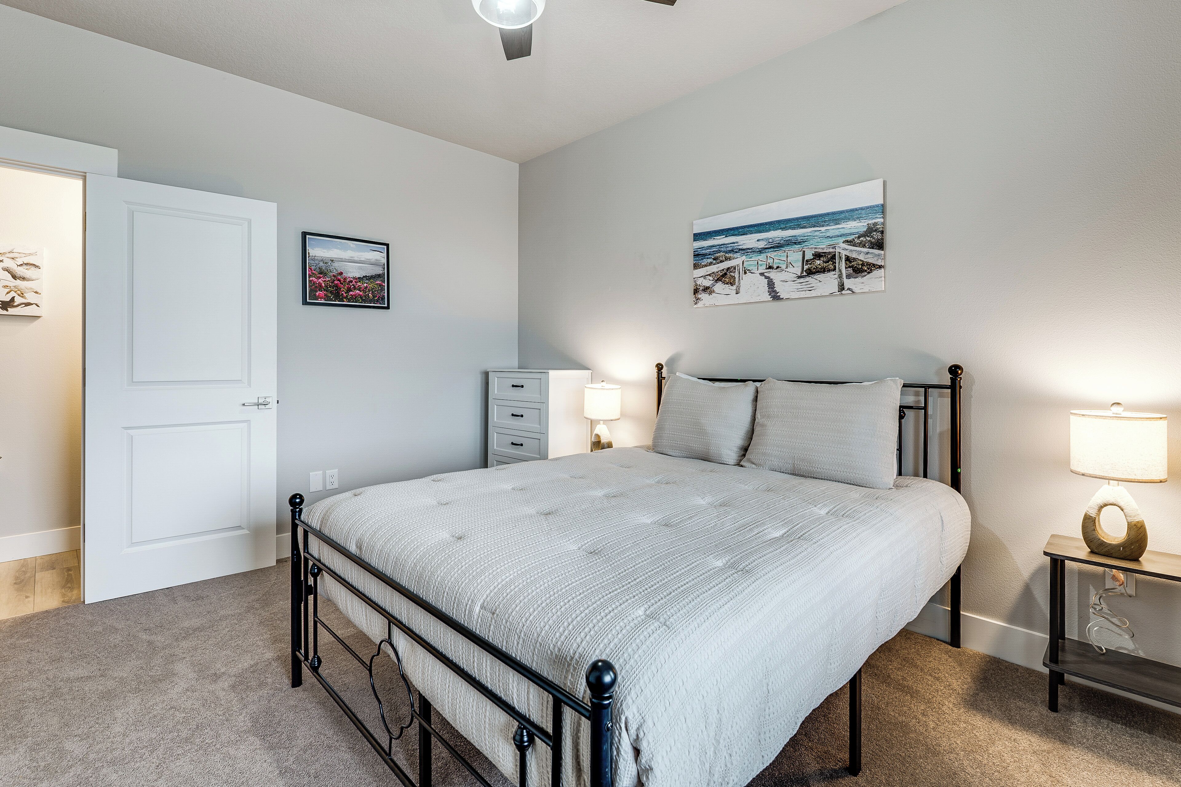 A bedroom with a bed, bedside tables, a nightstand, a door, and a wall-mounted picture.