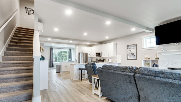 A modern living room with a grey sofa, a staircase, and a kitchen area with white cabinets and a flat-screen TV. - Walk to Marina! River-view Retreat in Hammond (Hammond)