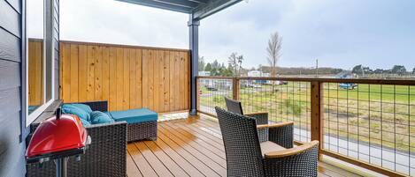 Une terrasse extérieure couverte, aménagée avec des meubles en osier, un barbecue et offrant une vue sur un champ verdoyant.