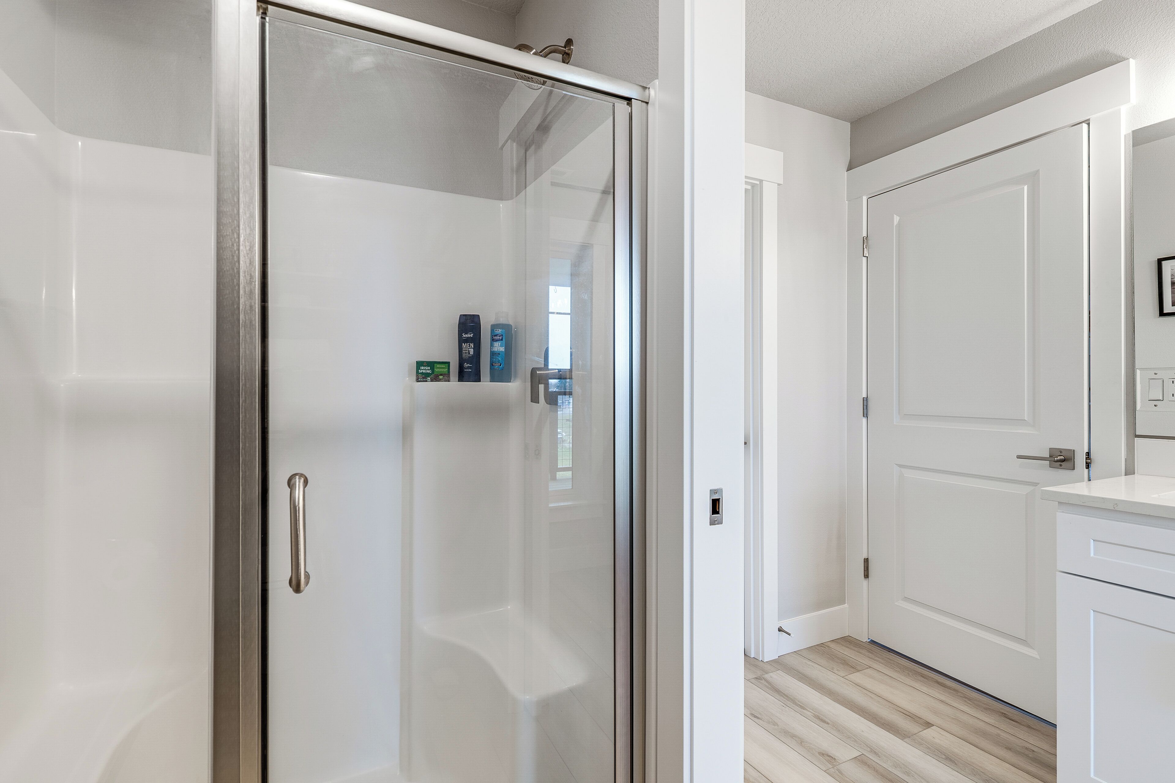 Une salle de bain moderne avec une douche à parois de verre, des meubles blancs et un plancher en bois.