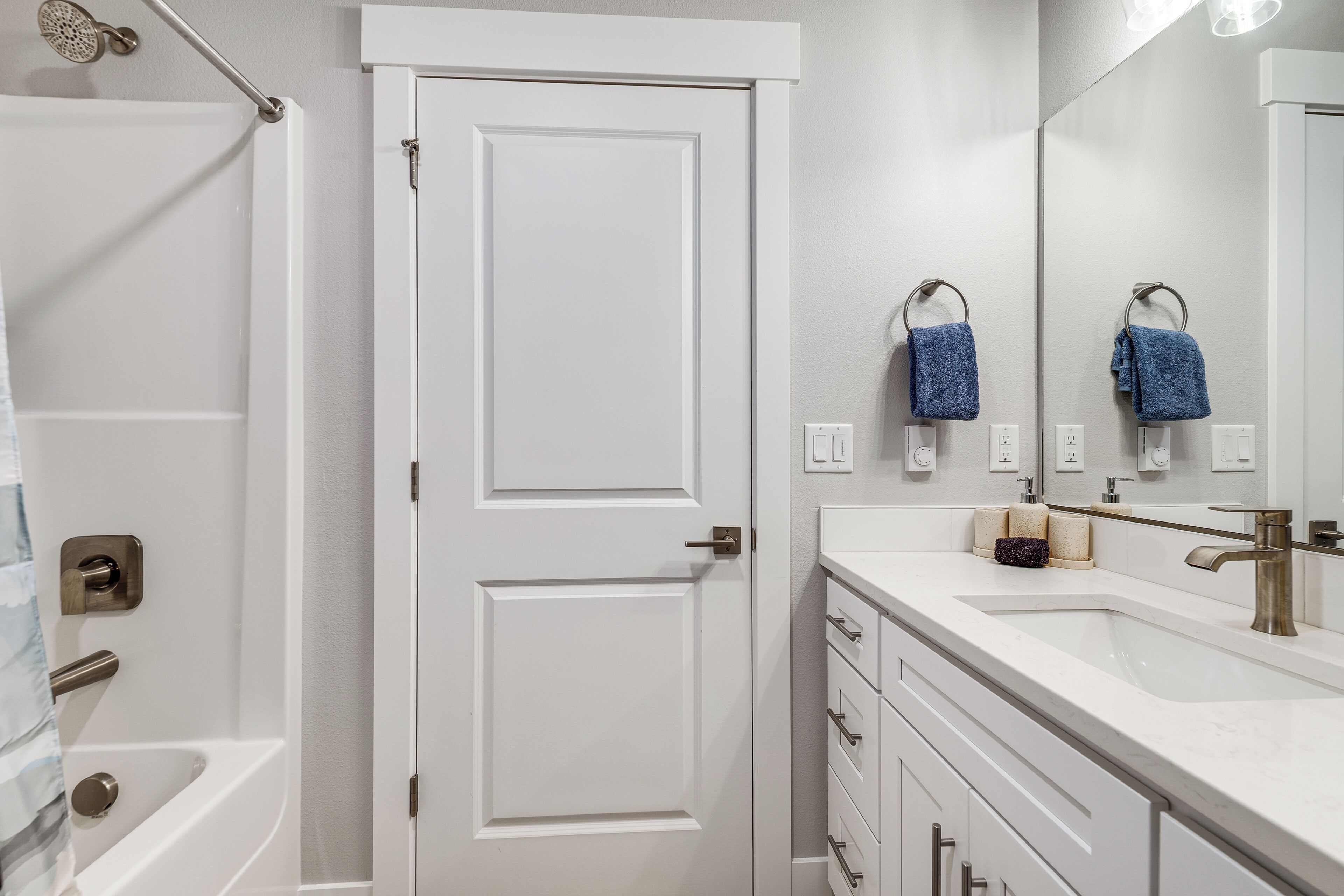 A bathroom with a white door, a bathtub, a sink with a mirror, and a towel rack.
