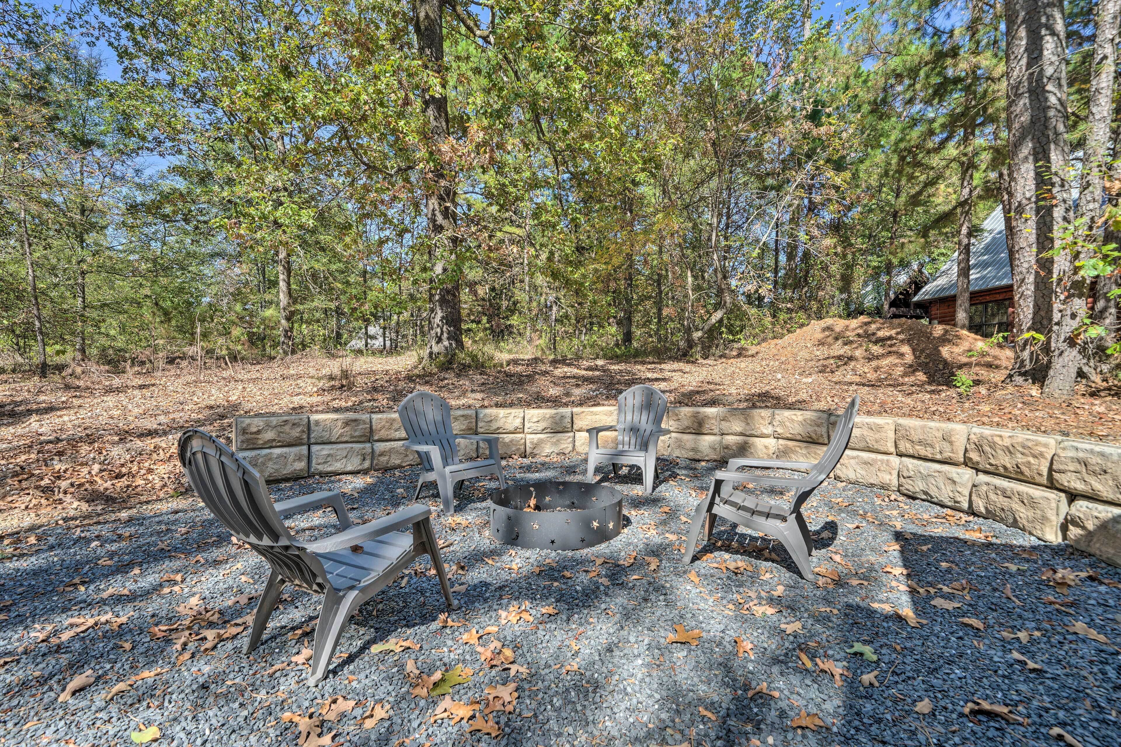 A fire pit area with Adirondack chairs, surrounded by a stone wall and trees.