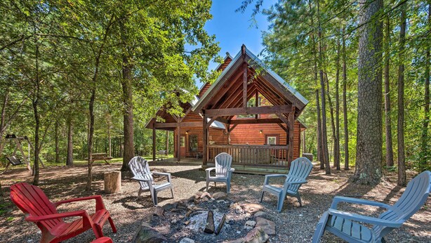 Une cabane dotée d’une terrasse, entourée d’arbres, et aménagée avec des fauteuils Adirondack et un foyer.