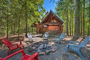 Eine Holzhütte mit einer Terrasse, umgeben von Bäumen, ausgestattet mit Adirondack-Stühlen und einer Feuerstelle.