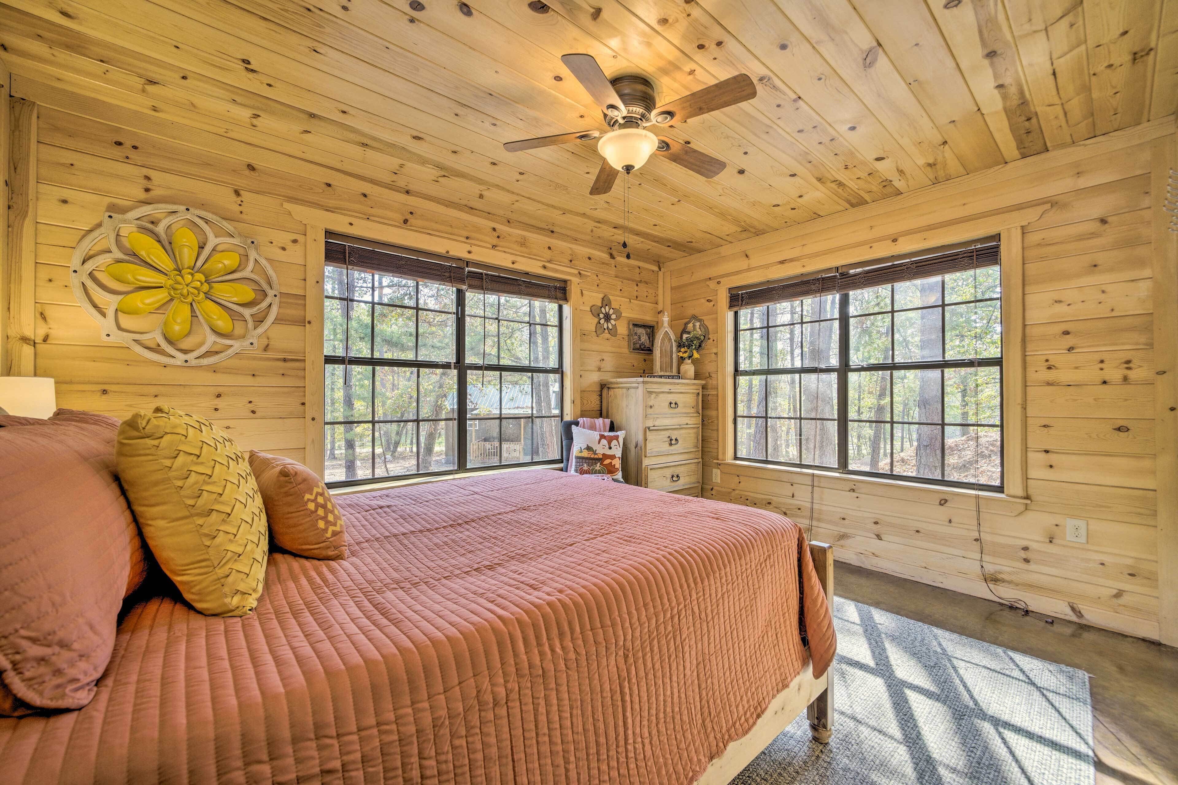 A wooden cabin bedroom with a bed, a ceiling fan, and large windows.