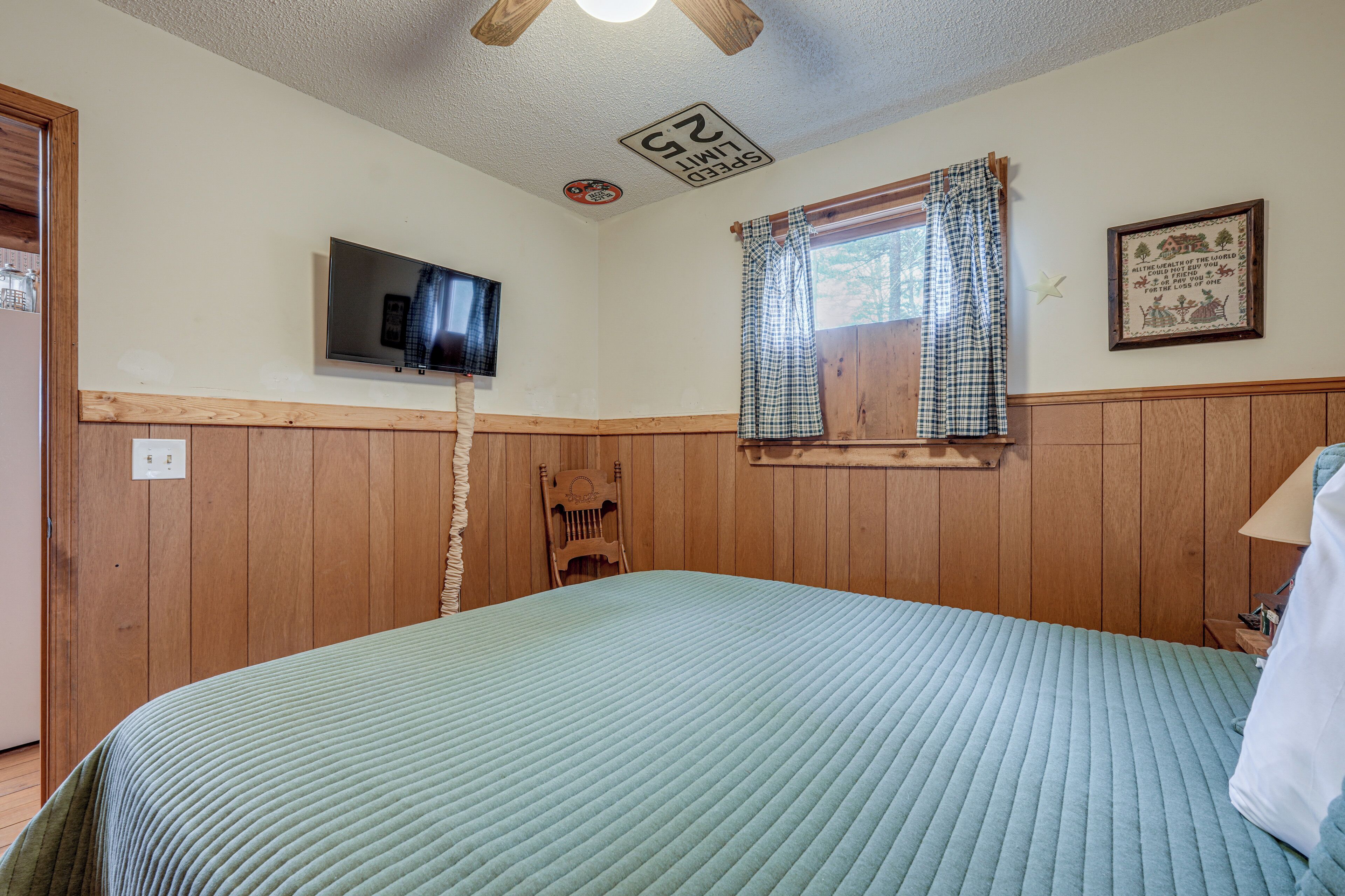 Une chambre à coucher comprenant un lit, un téléviseur, une fenêtre avec des rideaux, un plafond en bois et un panneau fixé au mur.