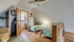 Une chambre avec un plafond en pente, des meubles en bois, deux lits, une armoire et un ventilateur de plafond.