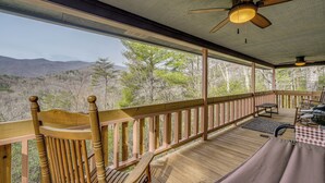 Une terrasse en bois avec un ventilateur de plafond, une nappe à carreaux et une vue sur les montagnes.