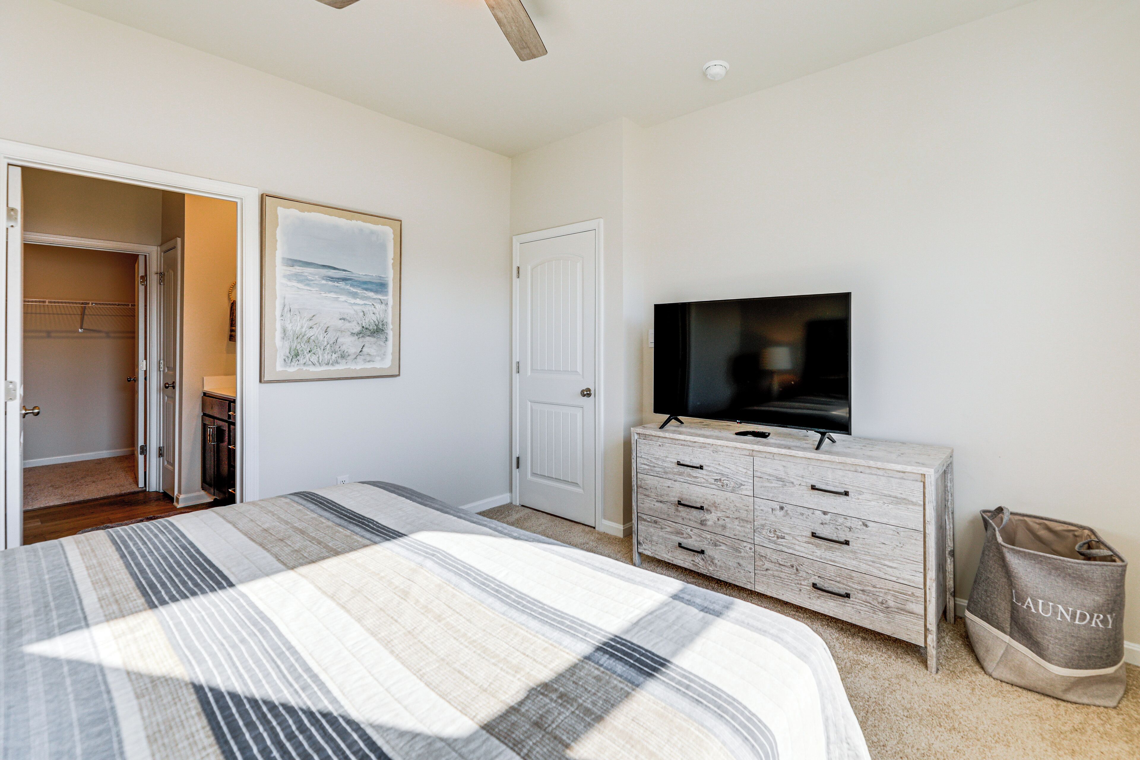 Une chambre à coucher comprenant un lit, une commode, un téléviseur et une porte donnant sur une autre pièce.