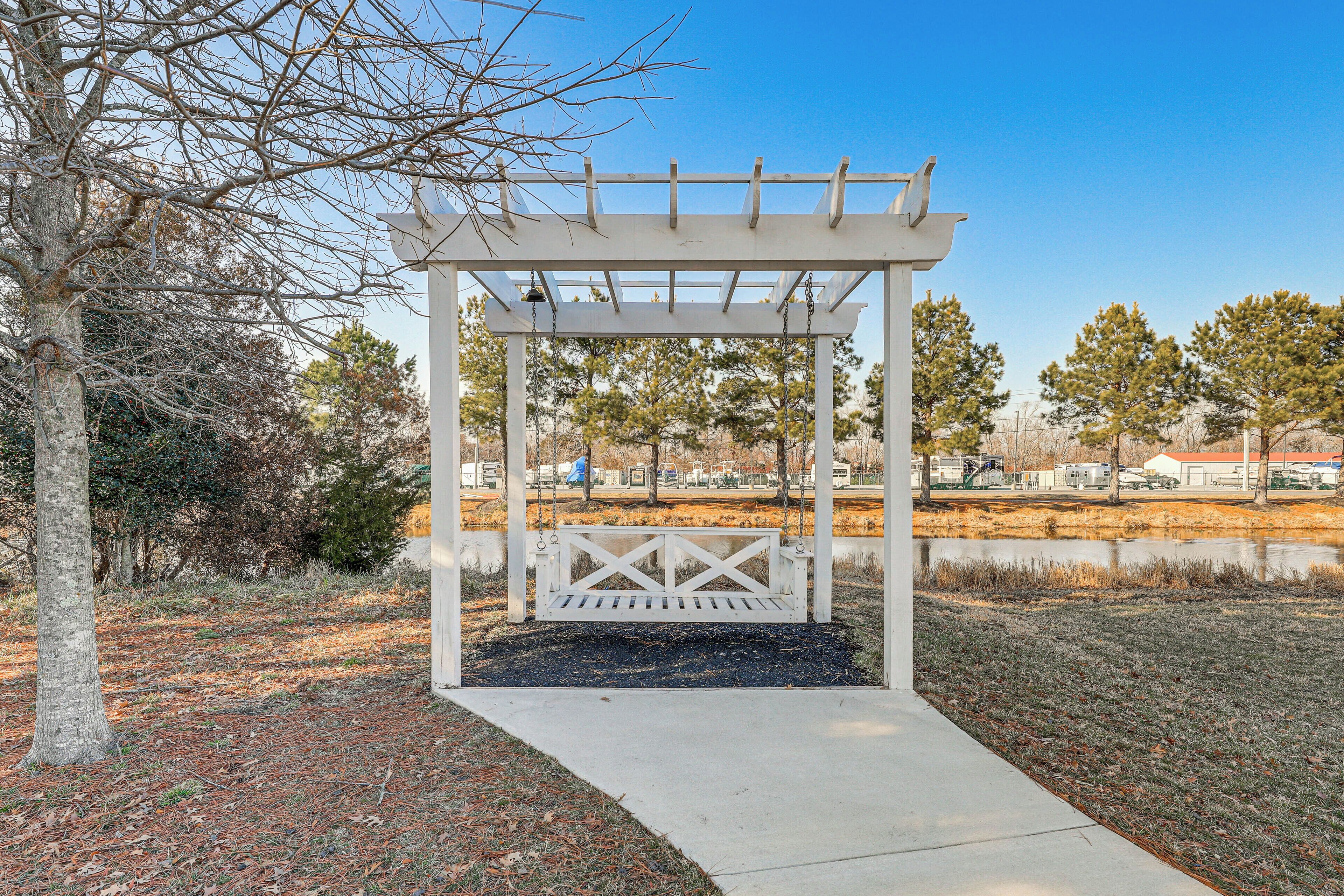 Une pergola blanche avec un banc, entourée d’arbres et sous un ciel dégagé.