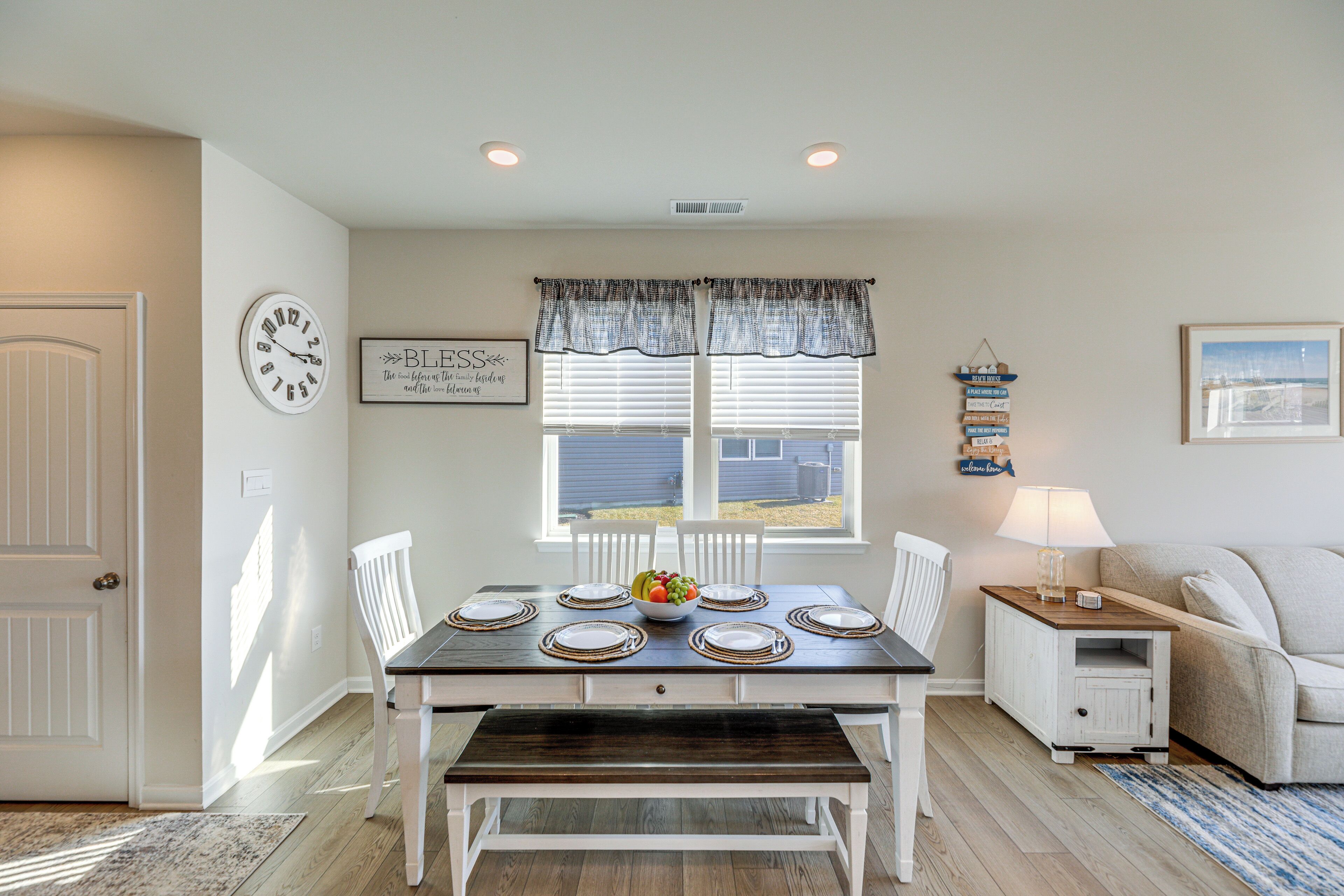 A dining area with a table set for four, a clock, and a window with blinds.