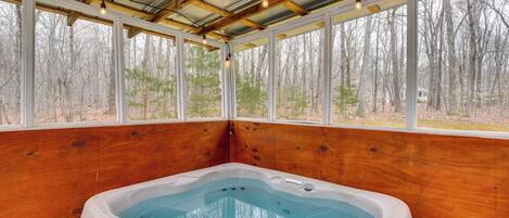 Un jacuzzi en una cabaña de madera con ventanas amplias y vistas a un bosque.
