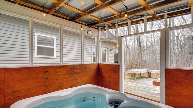 A hot tub in a covered outdoor area with wooden walls and large windows. - Family-ready Efland Home w/ Hot Tub + Deck (Efland)