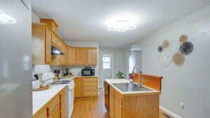 A kitchen with wooden cabinets, a microwave, a sink, and a ceiling light fixture. - Family-ready Efland Home w/ Hot Tub + Deck (Efland)