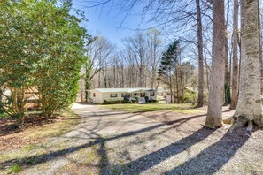 A single-story house with a front porch, surrounded by trees and a driveway.