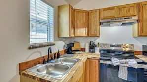 Una cocina con armarios de madera, un lavamanos de acero inoxidable, una estufa y una ventana con persianas.