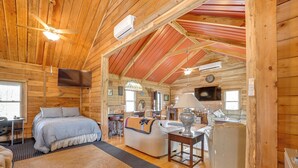 A log cabin interior with a bed, sofa, TV, and kitchenette. - Private Hot Tub! Country Retreat in West Virginia (Friendly)