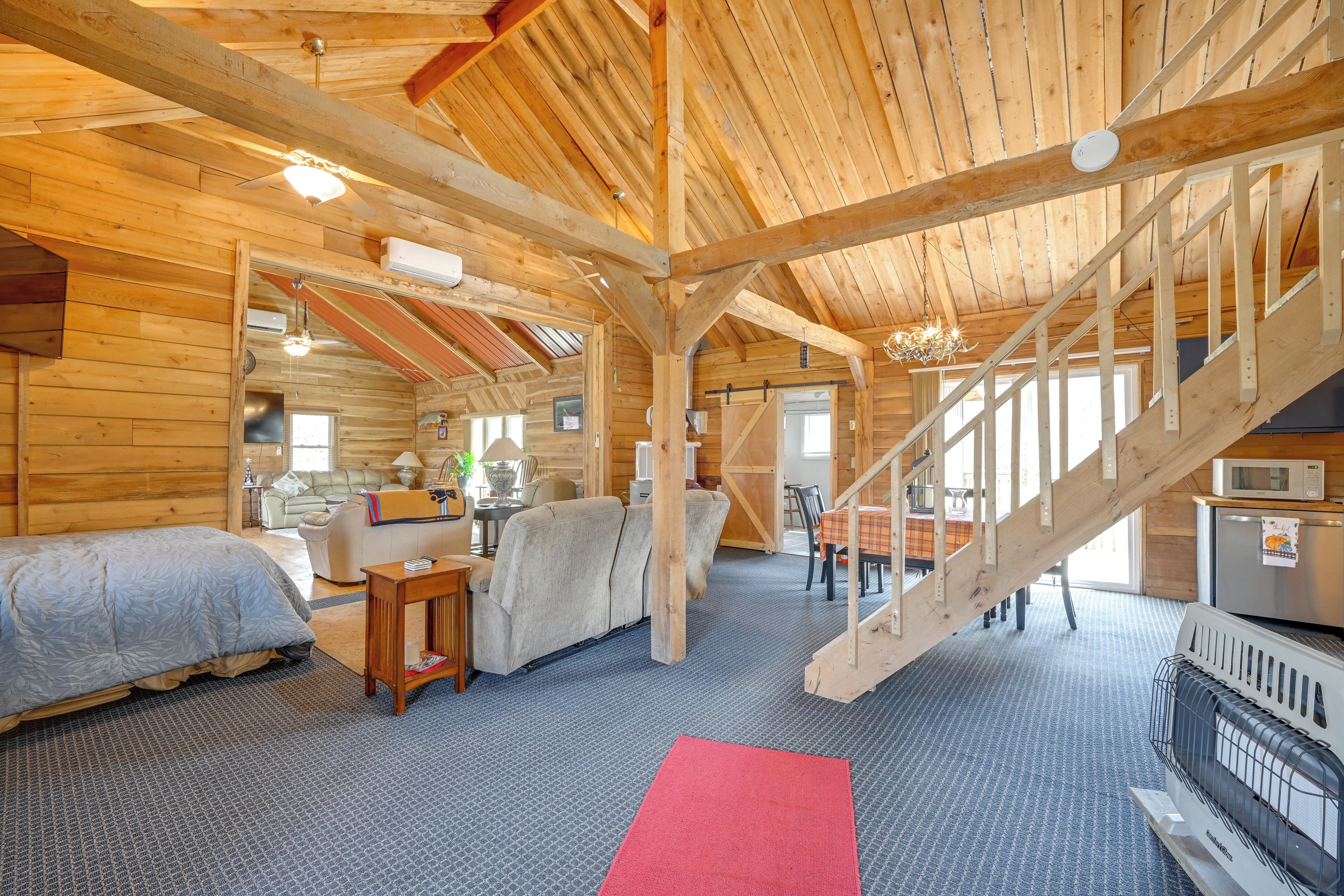 A log cabin interior with a staircase, a bed, a sofa, a dining table, and a kitchen area.