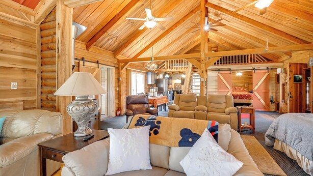 A log cabin interior with a high ceiling, wooden beams, a sofa set, a dining area, and a staircase. - Private Hot Tub! Country Retreat in West Virginia (Friendly)