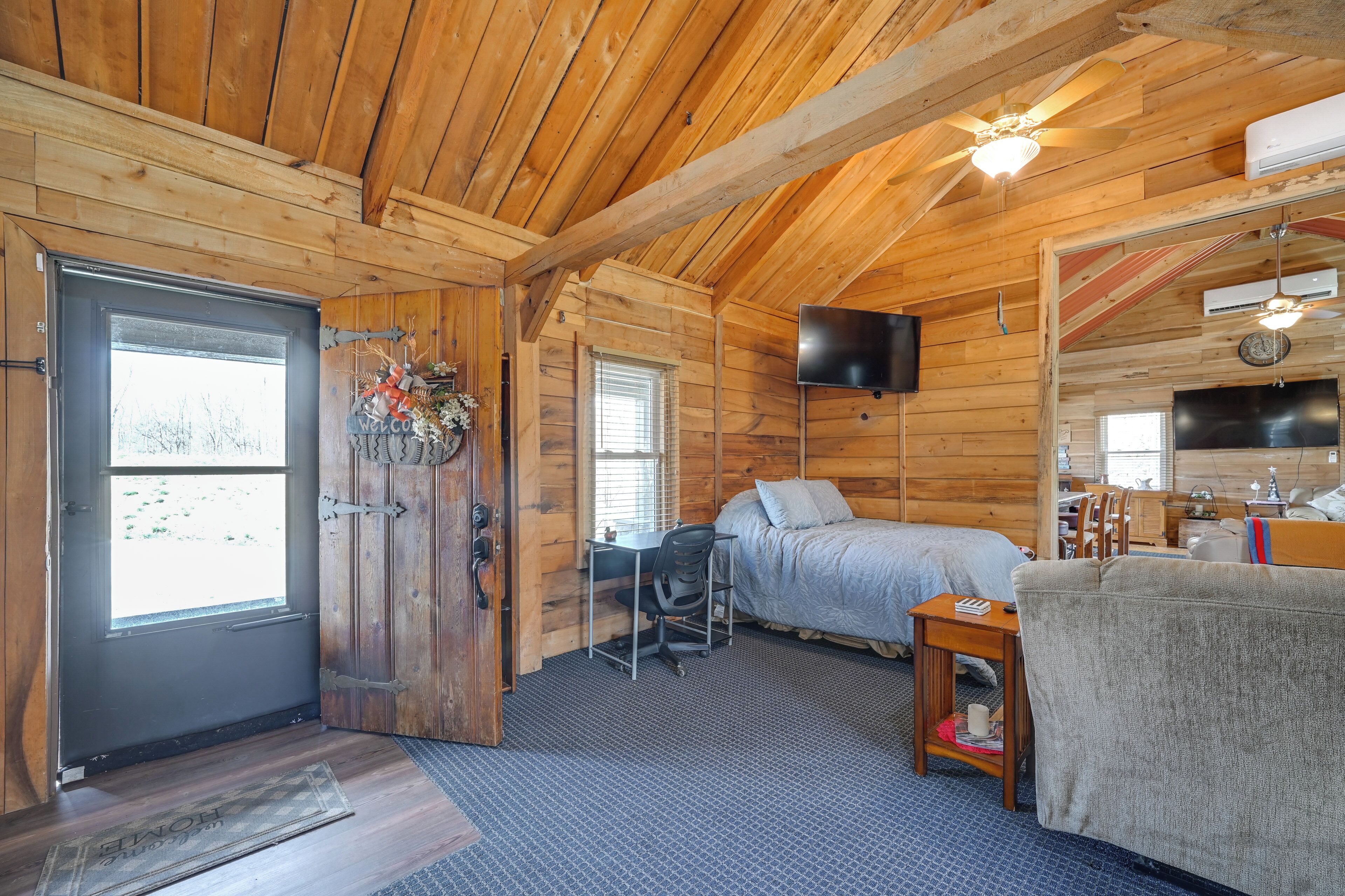 A log cabin room with a bed, desk, chair, TV, and a door leading outside.