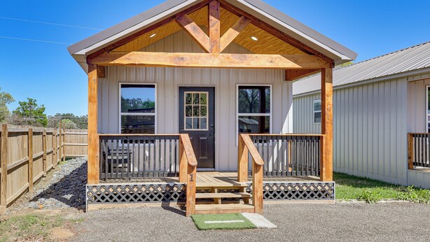 Un petit bâtiment en bois doté d’un porche, d’une porte d’entrée et de fenêtres.
