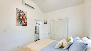 A bedroom with a bed, a door, an air conditioning unit, and a painting on the wall. - Piney Woods Tiny Cabin: 3 Mi to Sabine River! (Joaquin)