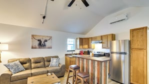 A modern kitchen with wooden cabinets, a stainless steel refrigerator, and a bar area. - Piney Woods Tiny Cabin: 3 Mi to Sabine River! (Joaquin)
