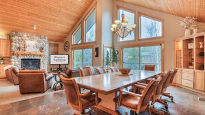 A spacious room with a large wooden dining table, comfortable seating, a fireplace, and large windows allowing natural light. - Luxury Sunriver Vacation Rental, Hot Tub, A/C, SHARC (Sunriver)
