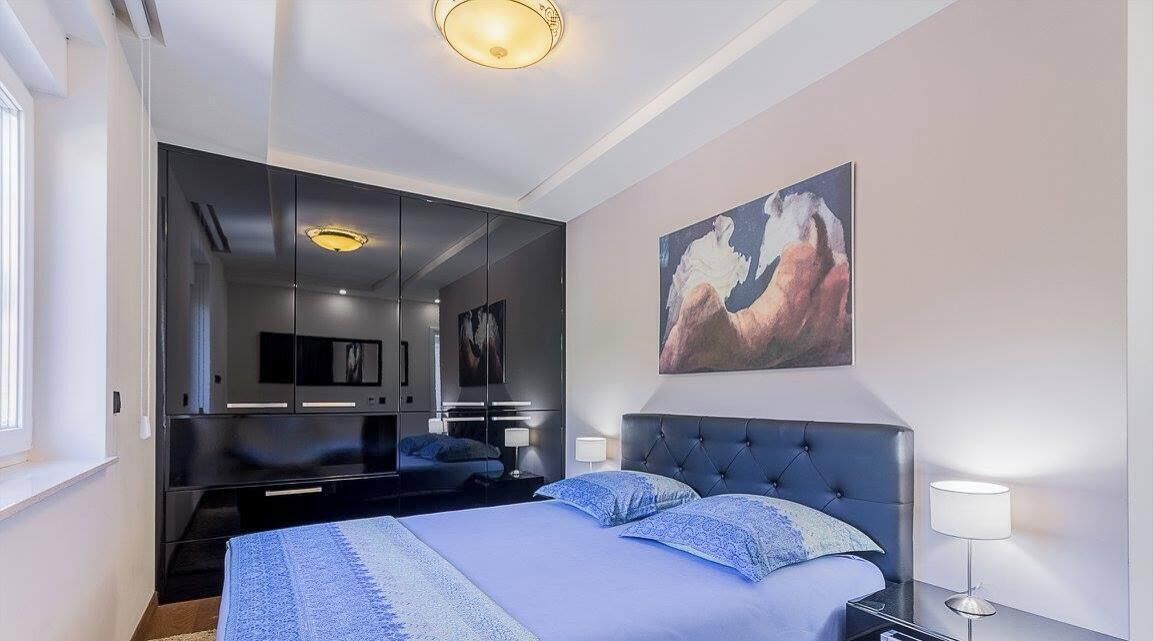 Ein modernes Schlafzimmer mit Bett, Nachttischlampen, einem großen Spiegel und einem Gemälde an der Wand.