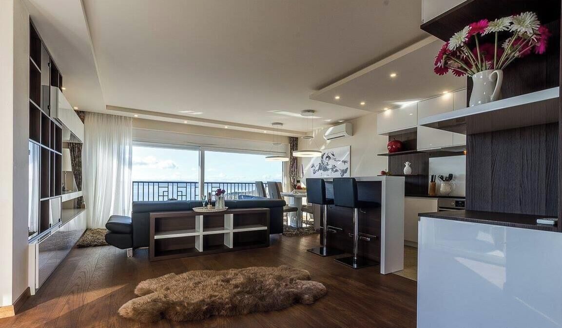 A modern living area with a sofa, dining table, kitchen, and a large window with a view.