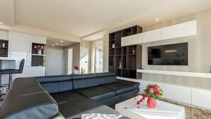 Een moderne woonkamer met een zwarte leren bank, een witte salontafel en een flatscreen televisie aan de muur.