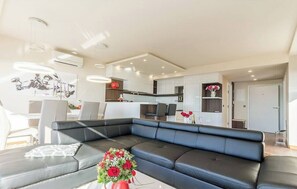 A modern living room with a black leather sofa, a dining area with chairs, and a kitchen in the background. - Modern apartment with sea view & pool in Klenovica (Klenovica)
