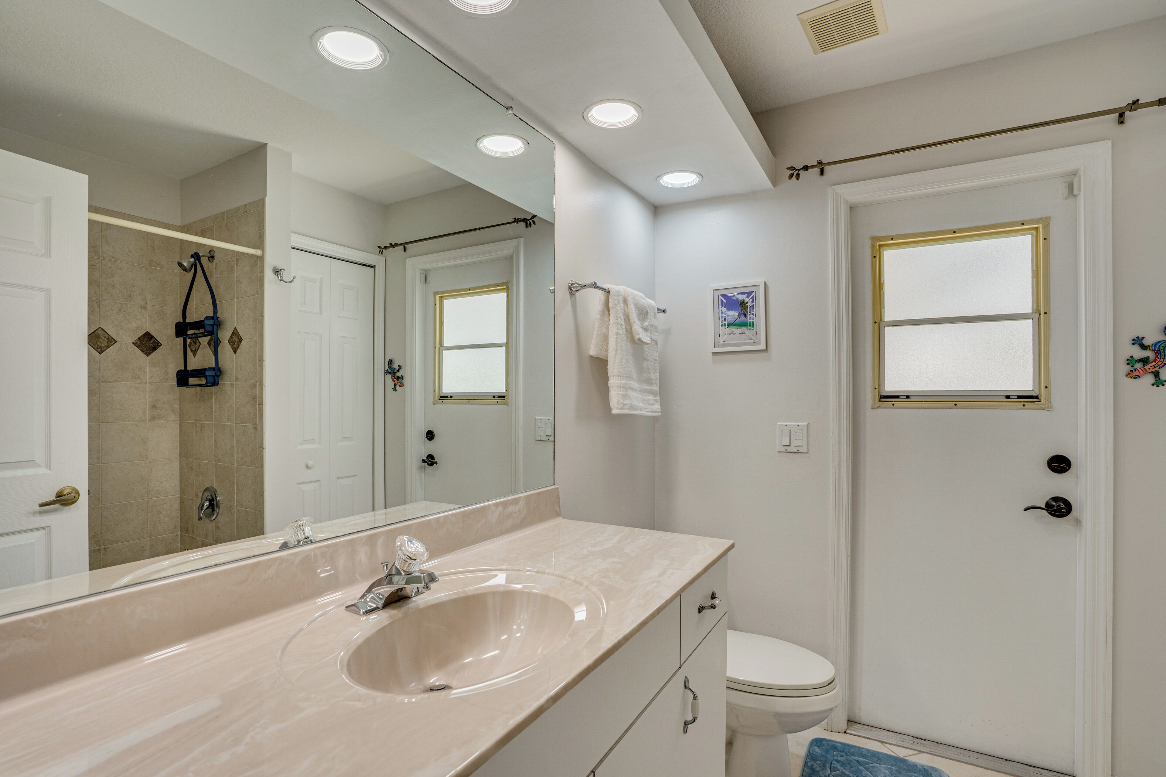 A bathroom with a large mirror, a sink, a toilet, and a shower area.