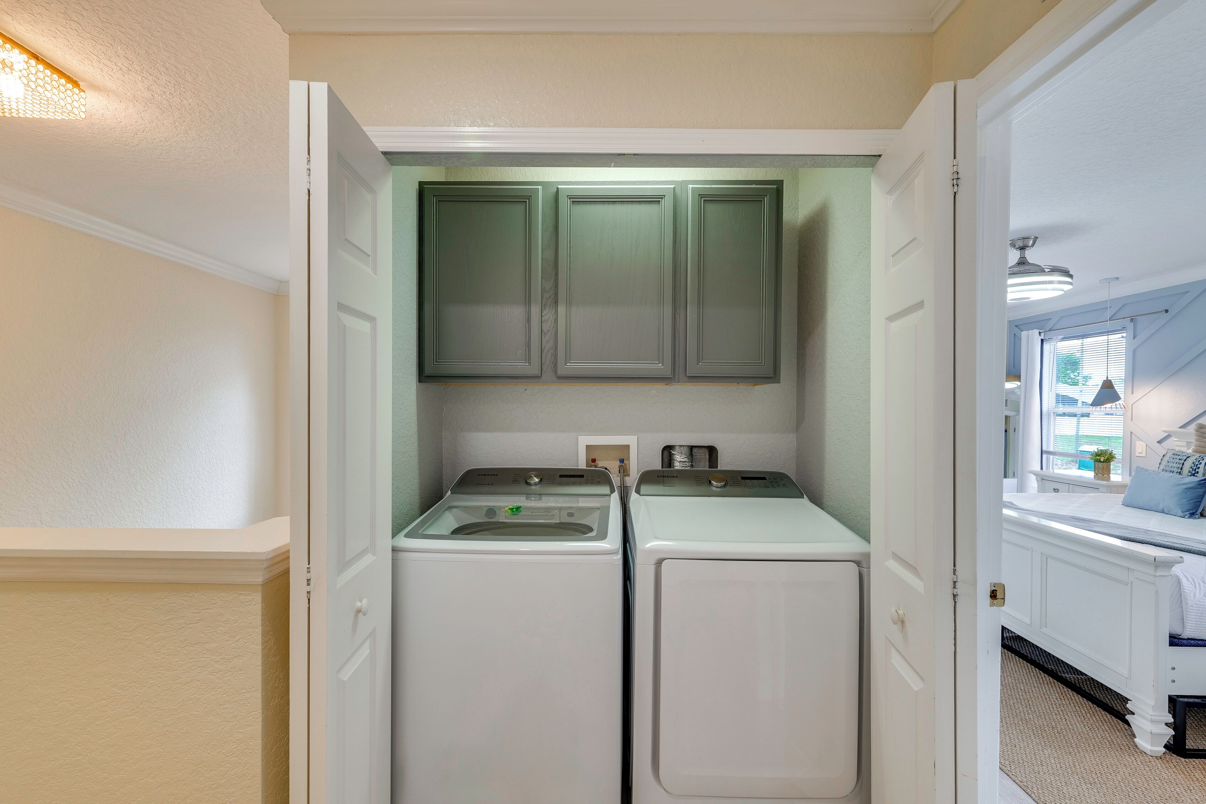 A laundry room with two washing machines and cabinets above.