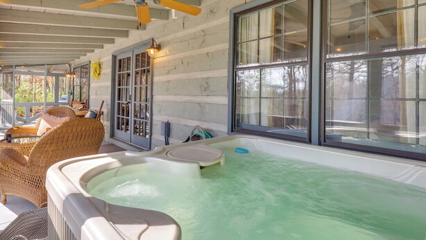 Ein Whirlpool in einem überdachten Außenbereich mit Korbmöbeln und großen Fenstern.
