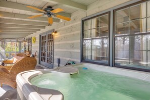 A hot tub in a covered outdoor area with wicker furniture and large windows. - 'peace of Aska' Cabin w/ Hot Tub & Fire Pit! (Blue Ridge)
