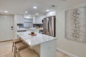 A modern kitchen with a large island, stainless steel appliances, and a decorative wall piece. - Sleek, Oceanfront Unit in Daytona Beach Shores! (Daytona Beach Shores)
