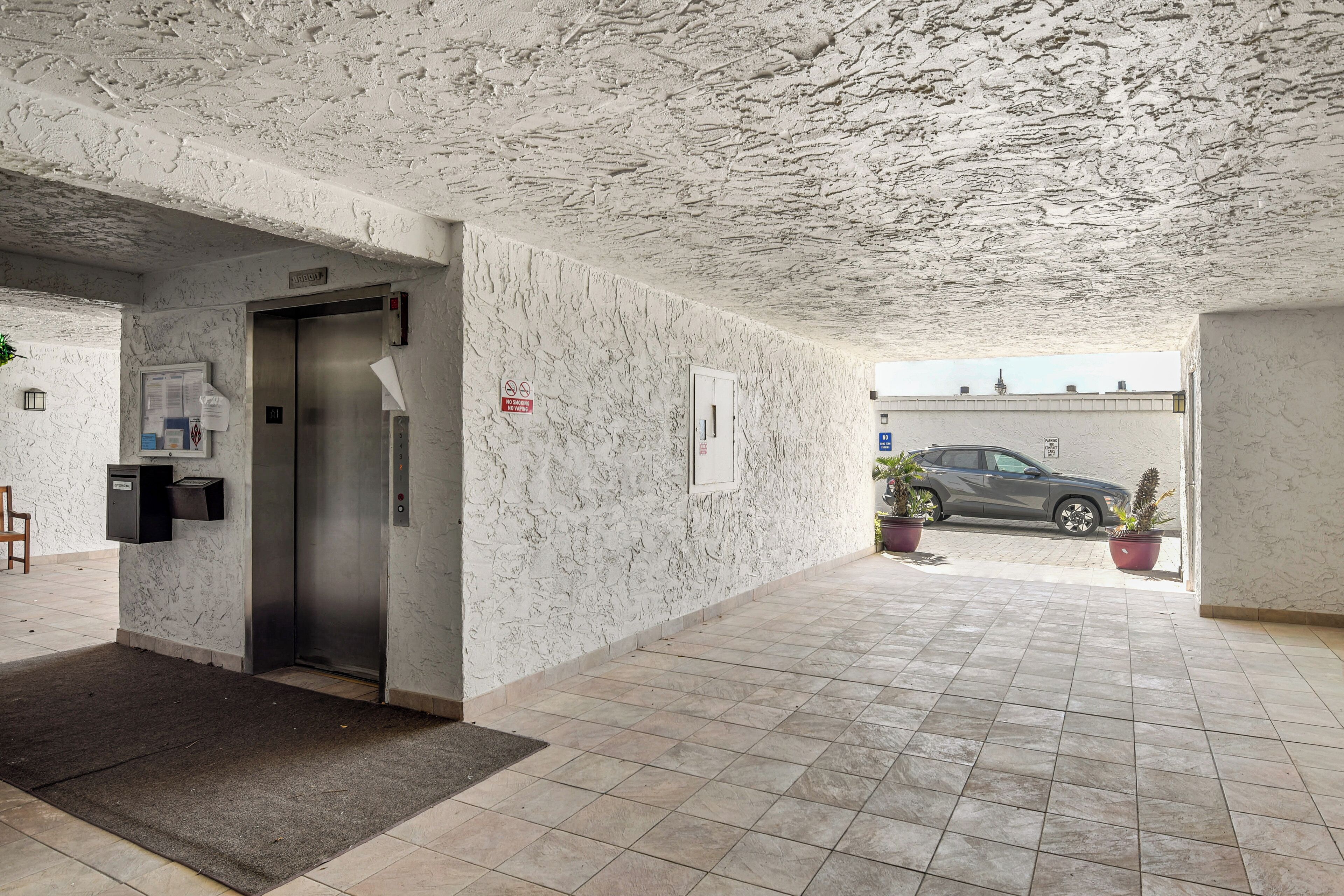 Un espacio interior con techo texturizado, una puerta que da a un ascensor y suelo de baldosas.