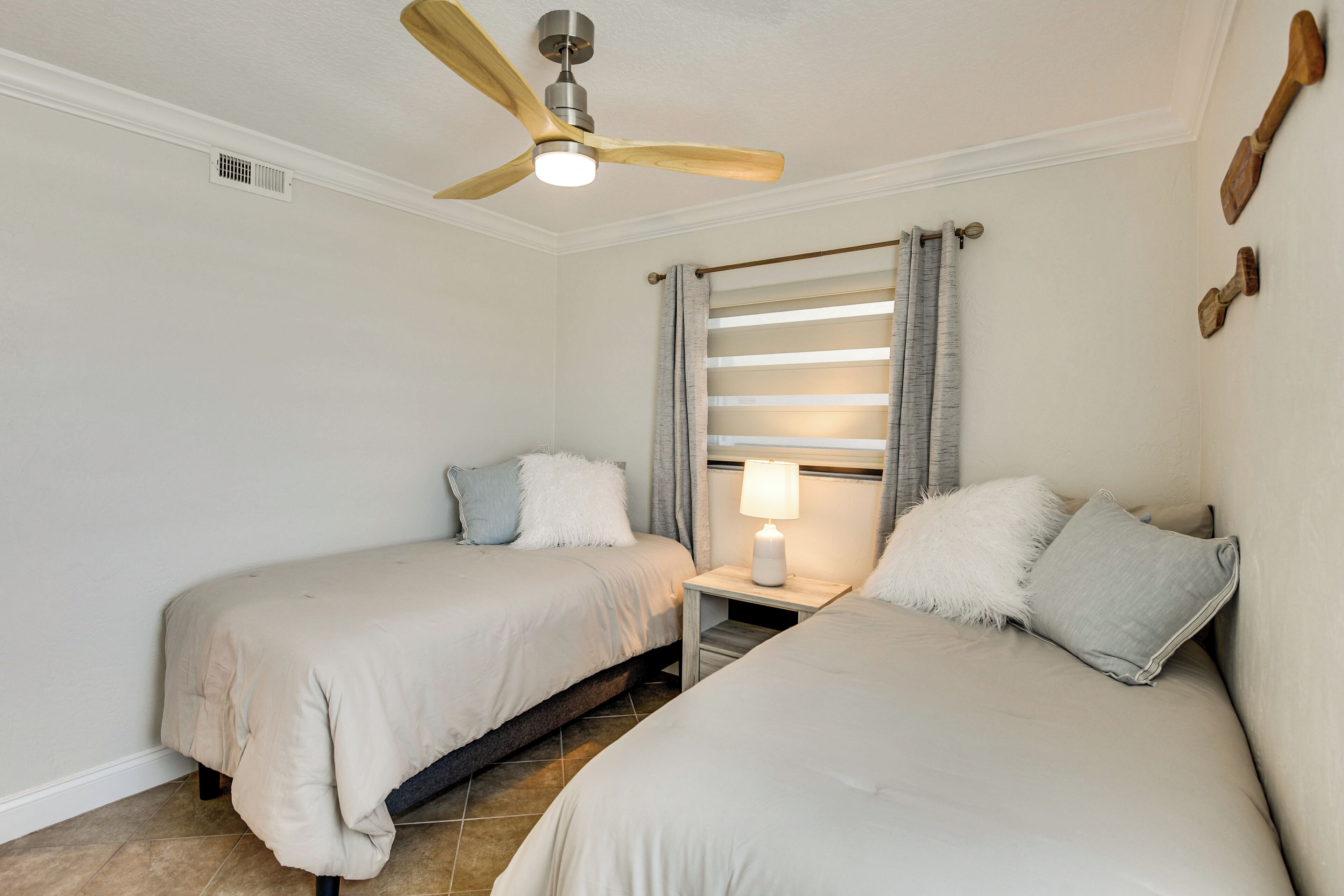 A bedroom with two beds, a ceiling fan, a nightstand with a lamp, and a window with curtains.