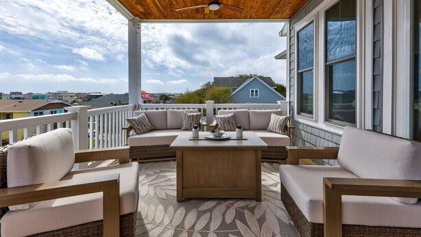 Eine überdachte Veranda mit Holzboden, einem weißen Geländer, einer beigen Sofagarnitur und einem Holztisch.