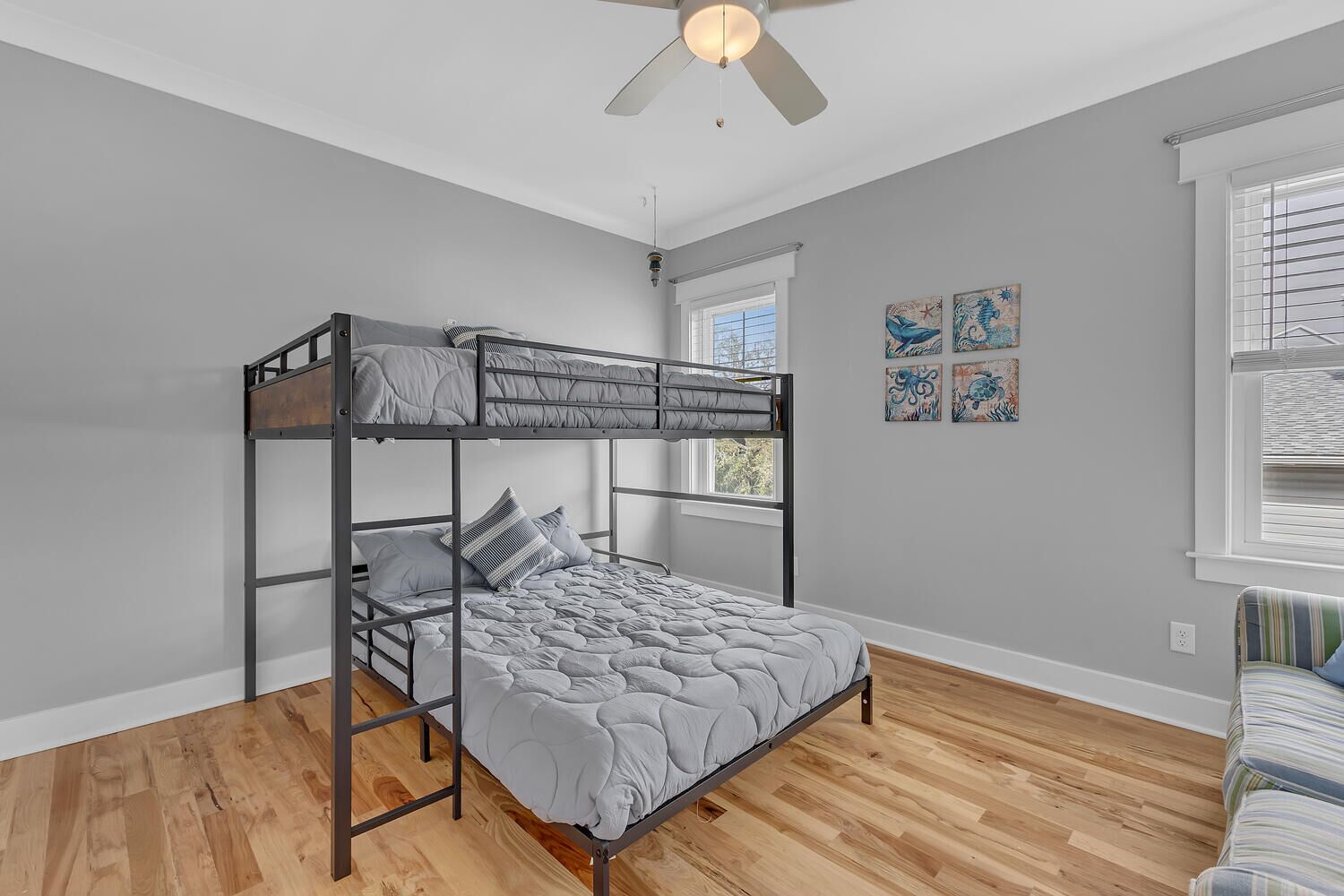 A bunk bed with a grey quilt, a ceiling fan, and a window with blinds.