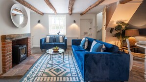 Ein Wohnzimmer mit Kamin, blauen Sofas, einem gemusterten Teppich und freiliegenden Holzbalken.