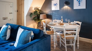 Ein gemütliches Zimmer mit einem blauen Sofa, einem Esstisch mit Stühlen und gerahmten Kunstwerken an der Wand.