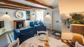 Ein gemütliches Wohnzimmer mit Kamin, blauem Sofa, Esstisch und einer großen Pflanze.